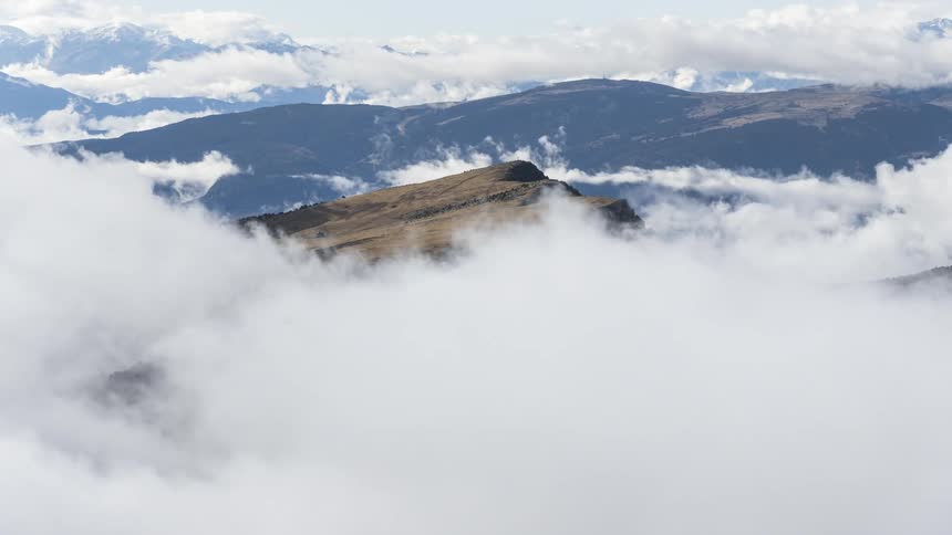 A mountain peak that is covered with a large dense white cloud passing to the left