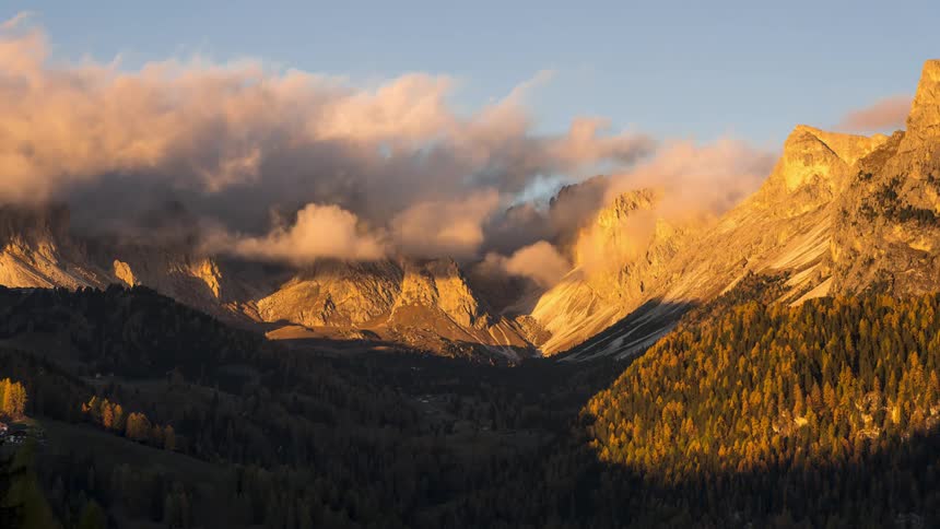 The setting sun casts shadows over the forested mountain