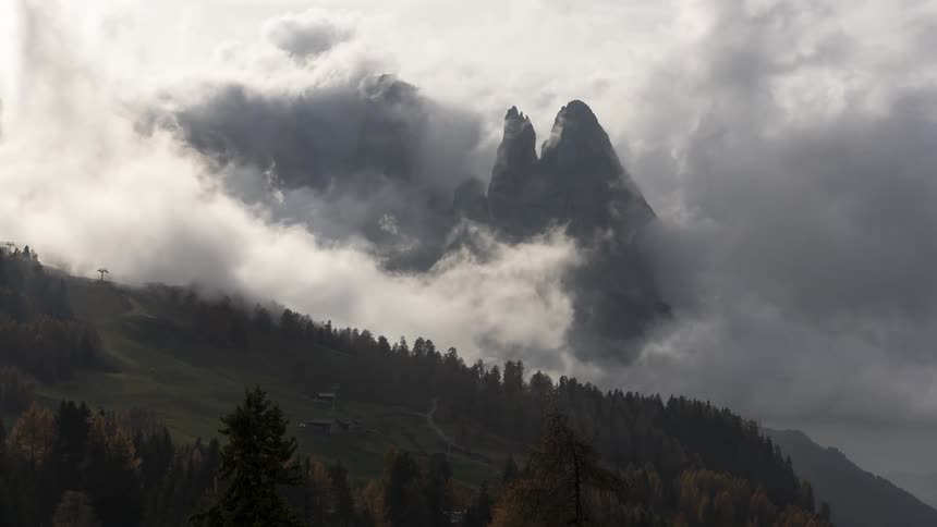 Farm occupies forest enclosed plateau near cloud covered mountain peaks