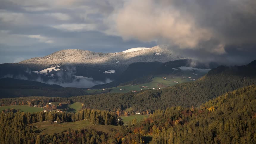 The dark clouds float over a forest and mountains