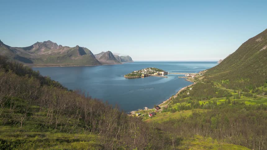 Serene natural landscape with a large body of water surrounded by green mountains and a small settlement on a peninsula