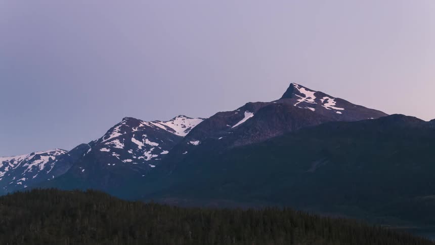 A mountain range with a snowcovered peak and it is getting dark