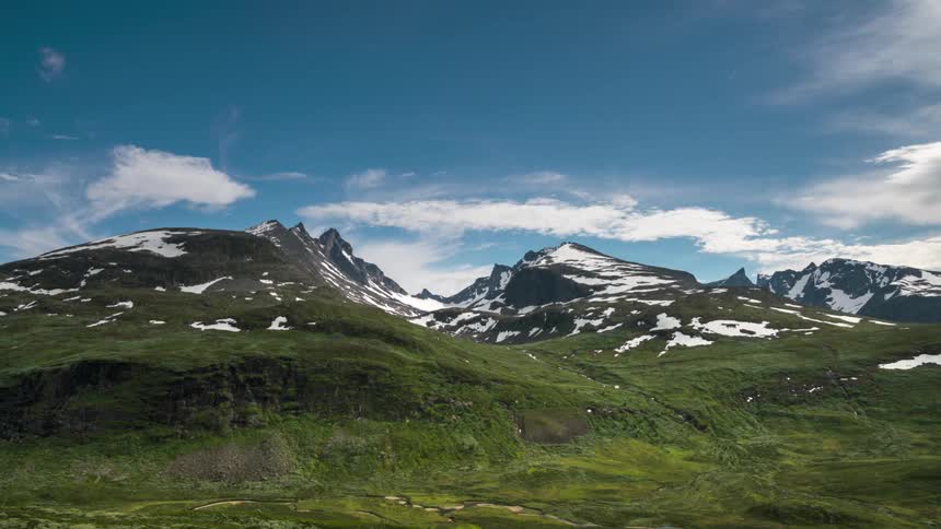 Greenish mountains with snowcapped peaks against a partly cloudy sky