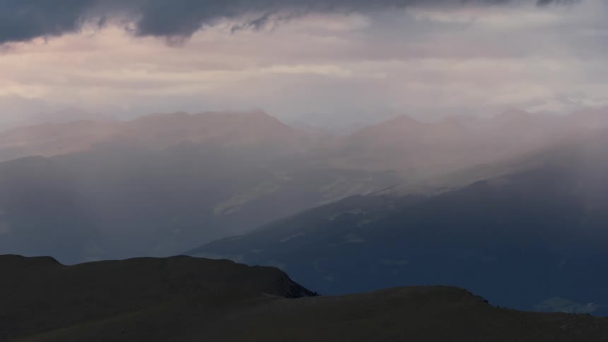 Wispy clouds float over mountains as the sun sets