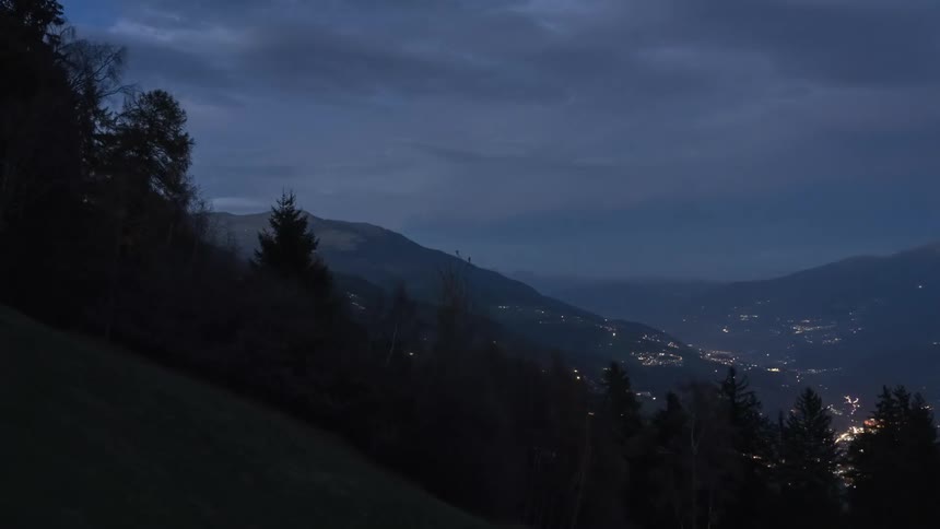 Silhouette of a mountain with conifers and lights of a city on the horizon