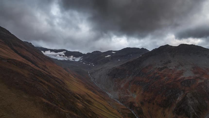 A valley between two mountains and many thin clouds passing through the sky quickly