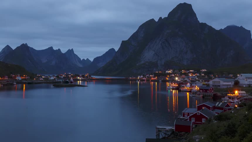 Time lapse of nightfall over a coastal town next to the mountains