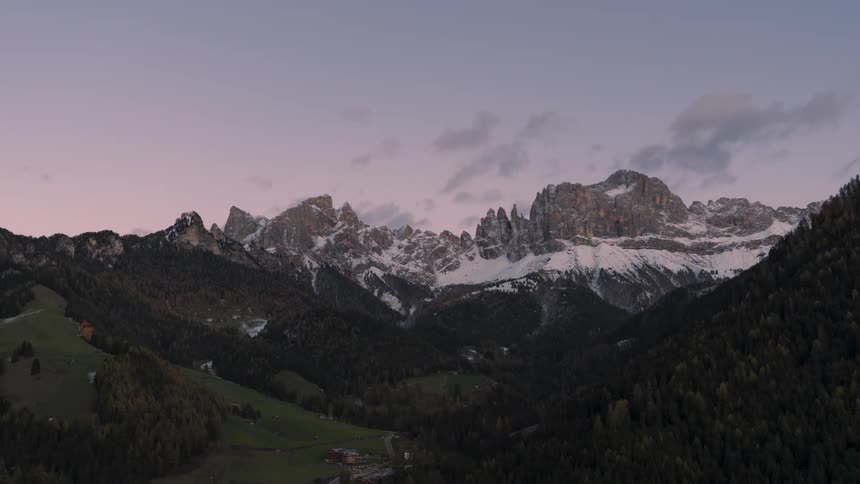 Green mountainous landscape with snowcapped peaks and the darkening day