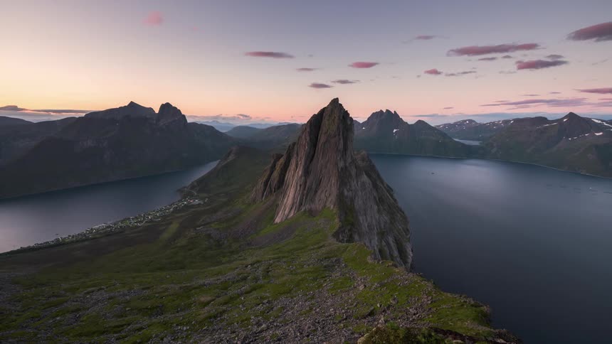 A small city on a coast lit up at night as clouds move over mountain ranges and water