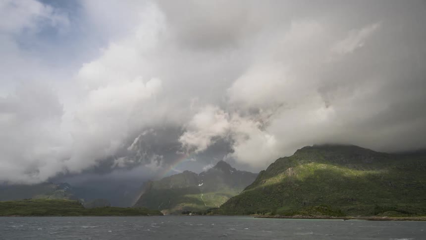 The clouds float over green mountains and a body of water