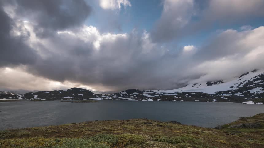 Dense overcast clouds passing above snowy mountains by the sea