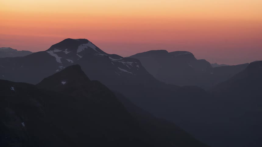 Orange sky changing to shades of purple above snowy mountains