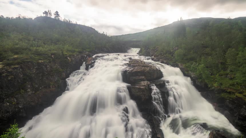 Time lapse of a river flowing down in the forest as clouds roll by