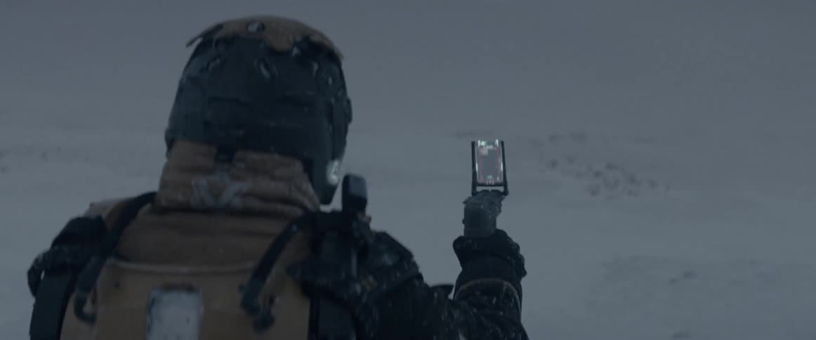 Person wearing helmet scans snow covered terrain with a hand held device during winter