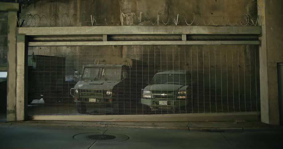 Two cars are parked in a fenced in area of a building