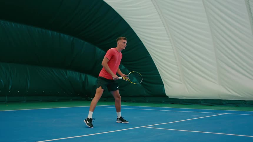 A man stretches while getting ready to play tennis on a court inside a tent