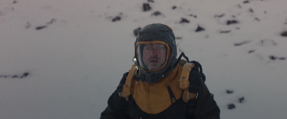 Man wearing a backpack and a helmet while standing on snowy terrain raises a handheld device