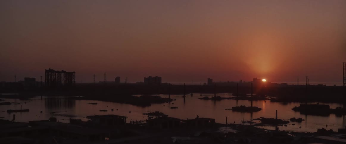 The sun sinks to the horizon over a marina on a coast