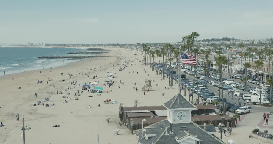 People walk on the beach and in a nearby parking area on a coast