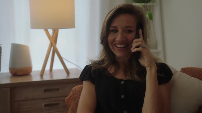 A woman sitting on the couch at home talking on a phone