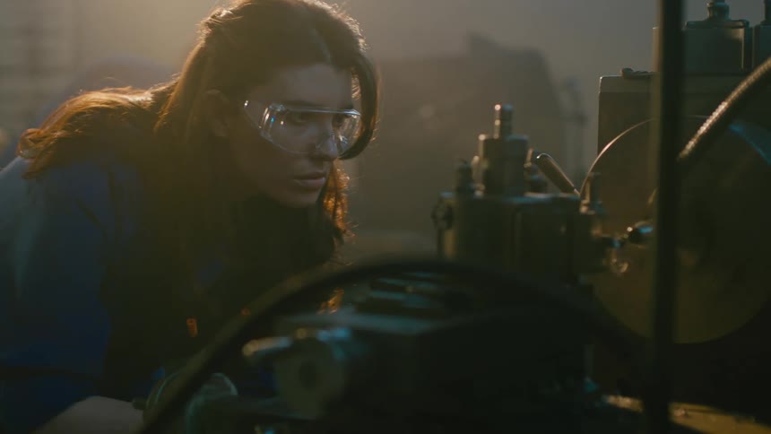 Blue collar worker wearing goggles operates machine in a workshop