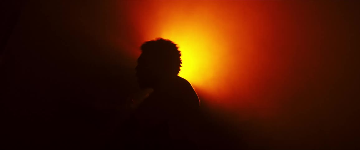 A black dancer in silhouette from a bright light performs dance moves