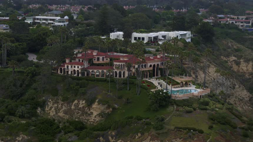 Aerial view of a luxurious property with a large redroofed house situated on a green hill