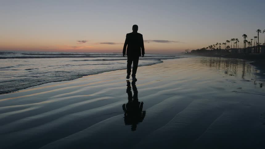 Silhouette of a man walking on the wet beach sand one morning