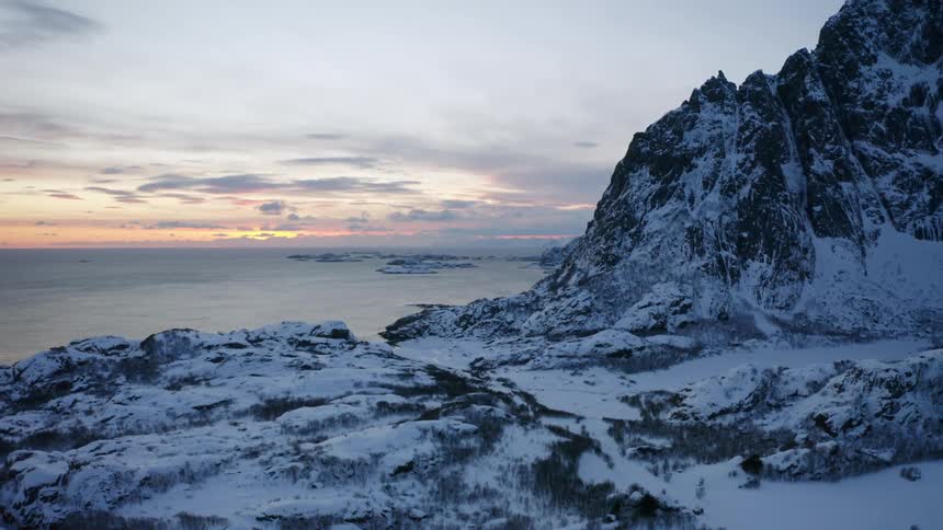 Landscape of snowcapped mountains by the sea against a reddish morning sky