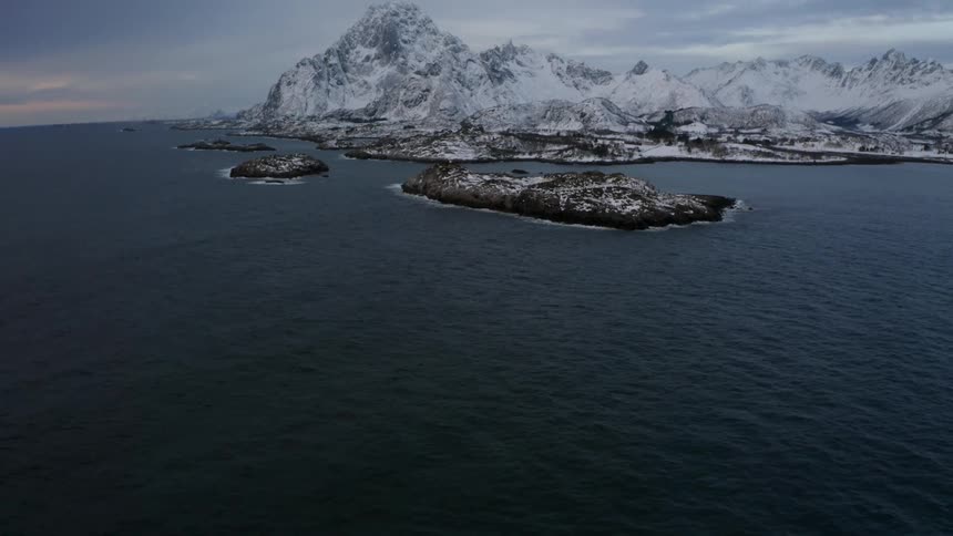A snowy mountainous landscape with the ocean in the foreground