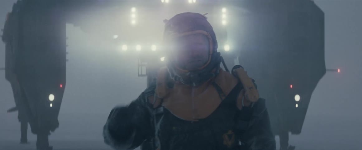 Man wearing a helmet standing in a foggy environment with bright lights in the background and holding a futuristic device