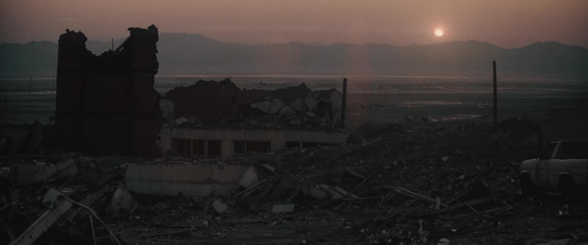 Sunset landscape illuminated by the sun low on the horizon with ruins and a damaged vehicle in the foreground with wreckage of a city
