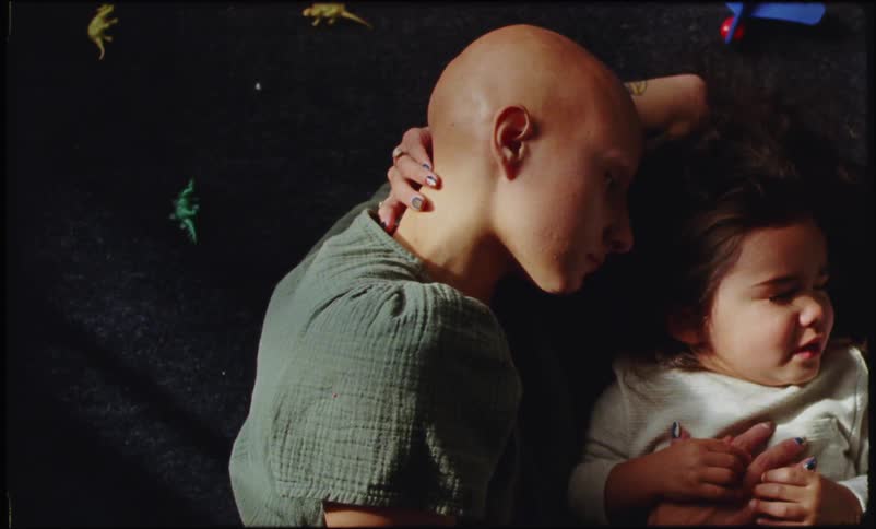 A bald woman and a child are lying down and the child is crying while looking away