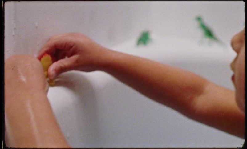 Small child playing with small dinosaur figures in the bath tub
