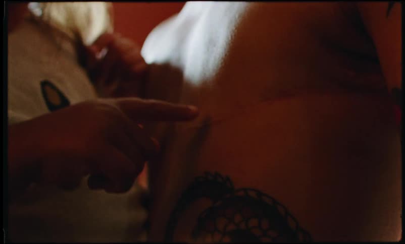 A girl touches the back of a shirtless tattooed person