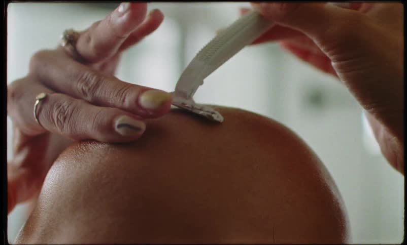 Close up of a woman shaving her head with a razor