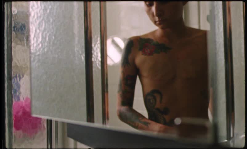 A tattooed bald person walking through a door and she has scars on her chest