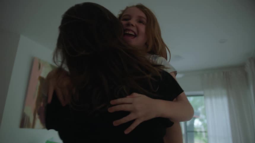 A daughter runs to her mother in a house and gets picked up and hugged