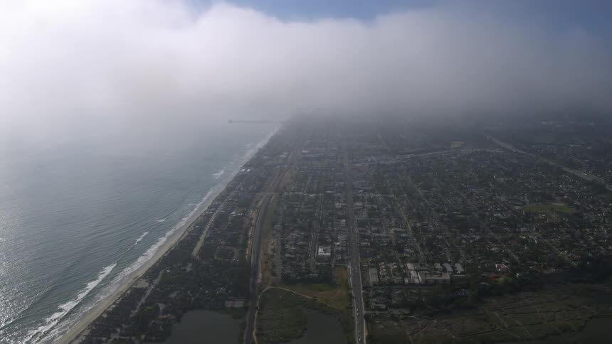 Dense white clouds float over an expansive city on a coastline