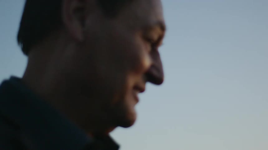 A man is smiling outdoors on a clear sky day and looks happy