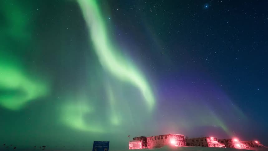 Arctic landscape with some warehouses in the background and a night sky with stars and northern lights