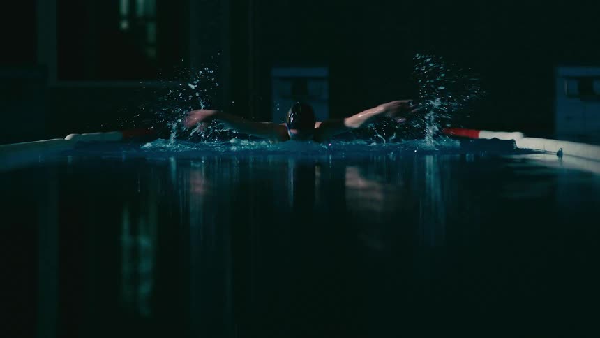 A swimmer doing butterfly is swimming up a lane towards the camera they are wearing a black cap and racing suit