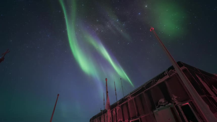 The northern lights illuminate the night sky with green streaks over a scientific research station