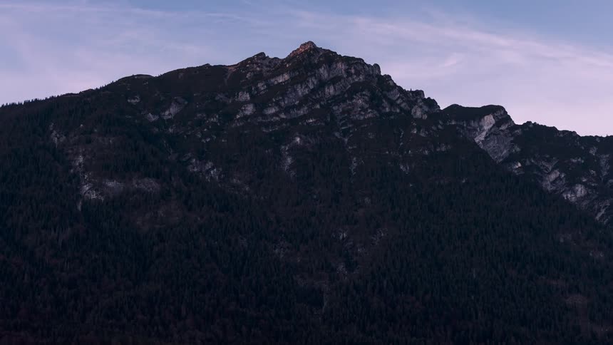 An airplane flies over a tall mountain covered in forests