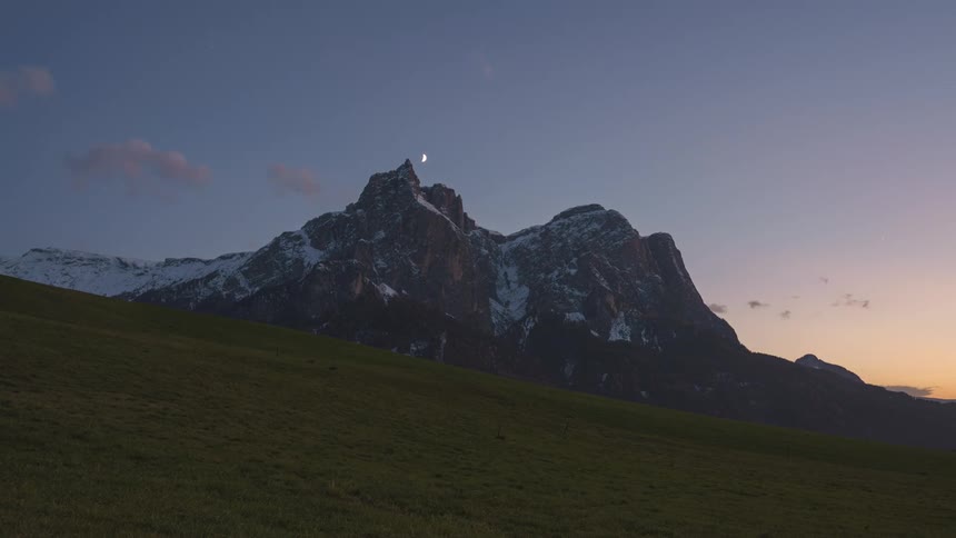 Vast green field with snowy mountains in the background and a sunset sky