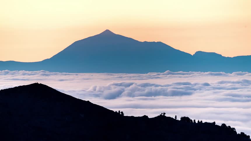 Time lapse of white clouds rolling at the base of a mountain at sunset