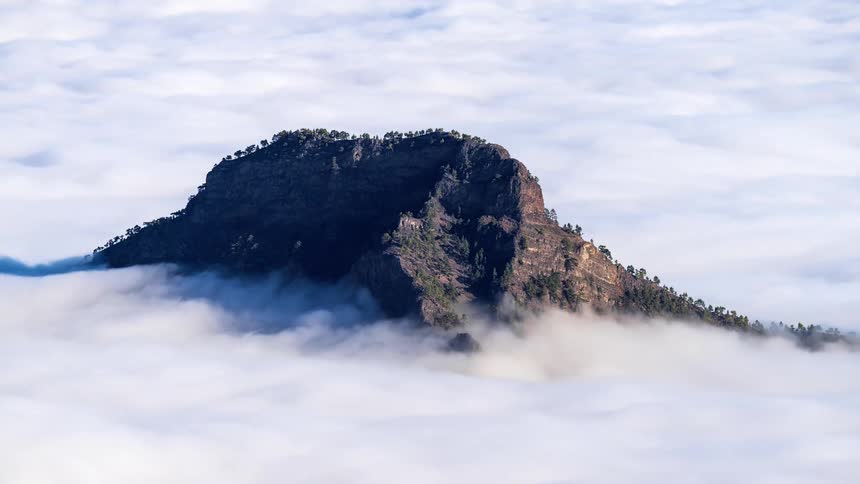 Time lapse of mountain peak emerging from a sea of clouds