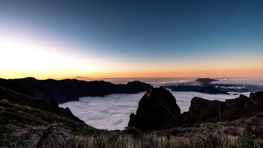 Time lapse of a sea of clouds rolling under mountain peaks from night time to daylight
