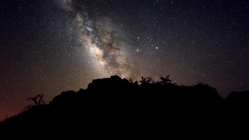 A silhouette of a location on a starry night with a nebula and time is passing quickly
