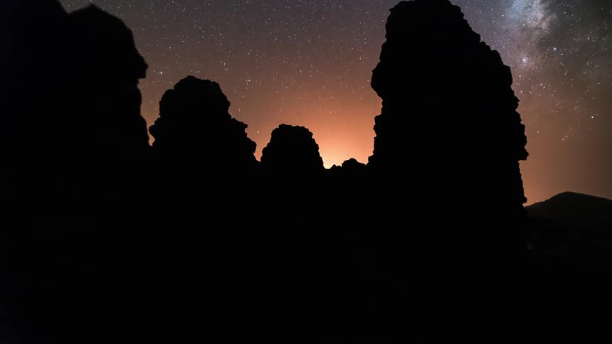 Time lapse of a shimmering glow behind tall rock formations under a starry sky